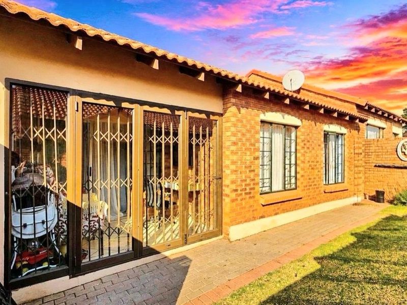 Rear view of a face brick townhouse featuring a paved walkway, security gates, and a small garden area under a sunset sky.