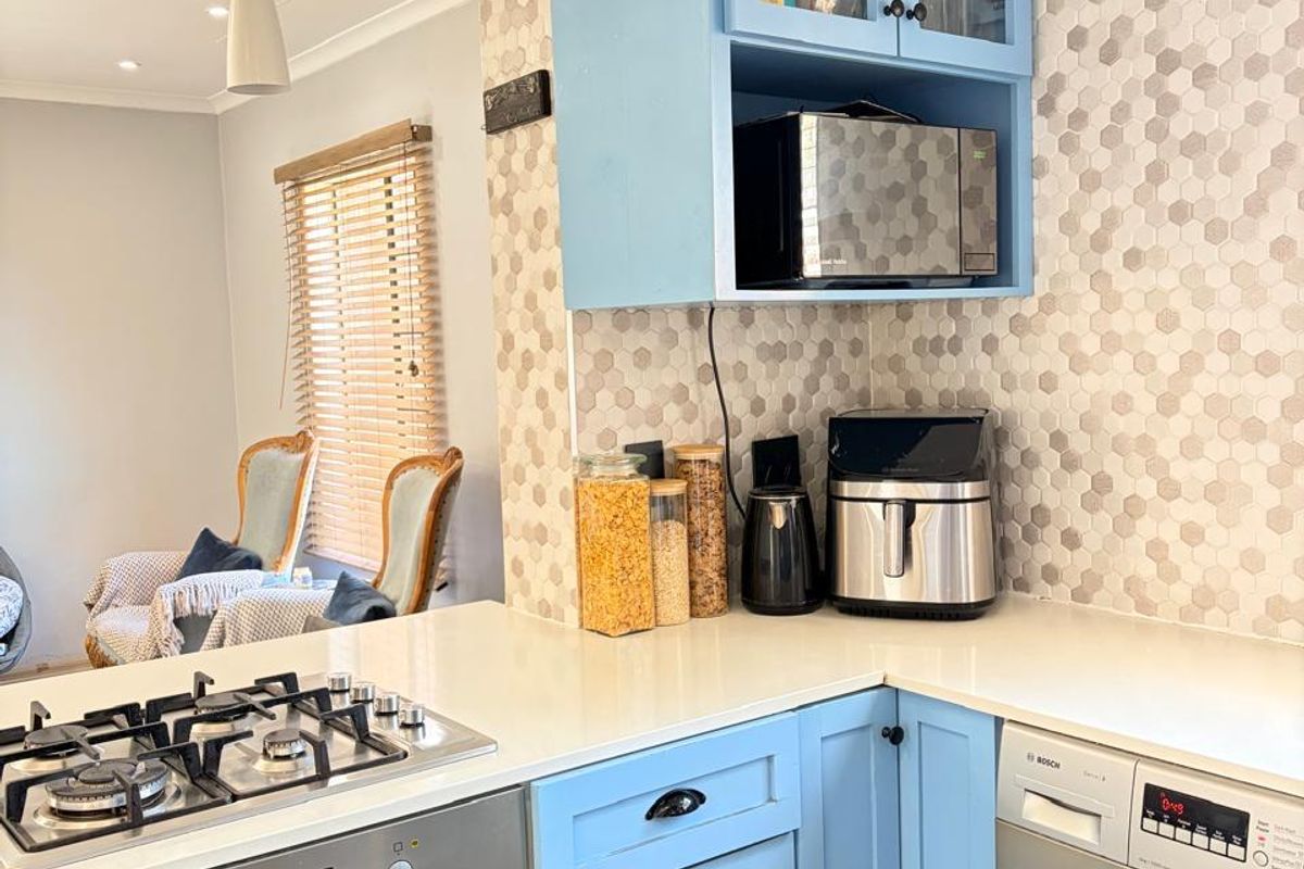 A functional kitchen featuring light blue cabinetry, stone countertops, a gas hob, built-in oven, and an integrated washing machine with a modern tiled backsplash.