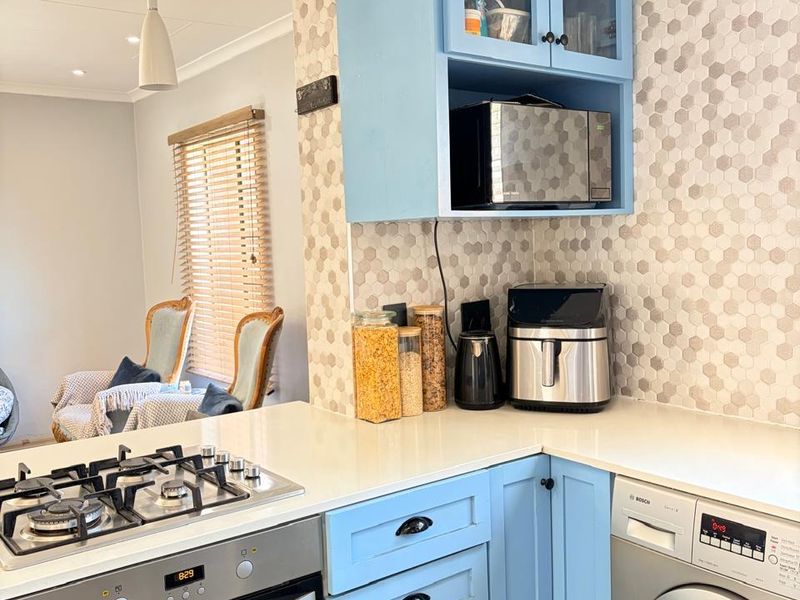 A functional kitchen featuring light blue cabinetry, stone countertops, a gas hob, built-in oven, and an integrated washing machine with a modern tiled backsplash.