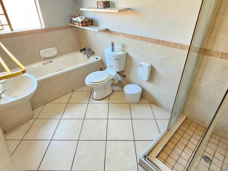 A functional bathroom featuring a bathtub, separate shower enclosure, toilet, and neutral wall and floor tiling.