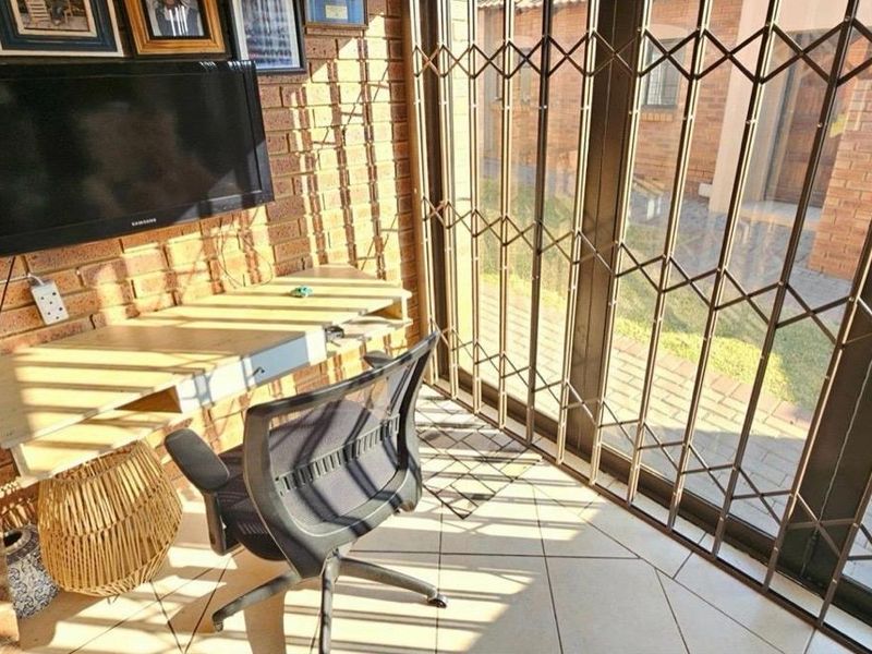 A home office space featuring exposed brick walls, ceramic floor tiles, and a sliding glass door with a security gate leading to the exterior.