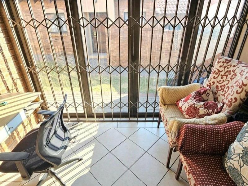 A sunlit living area featuring tiled flooring, a brick feature wall, and sliding glass doors secured with a metal gate.