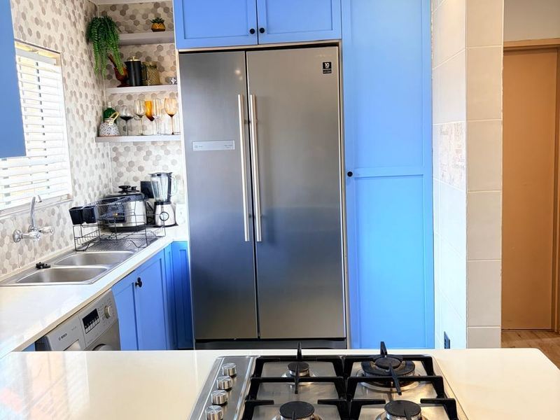 Modern kitchen featuring vibrant blue cabinetry, quartz countertops, a built-in gas cooktop, and a stainless steel double sink with a decorative tiled backsplash.