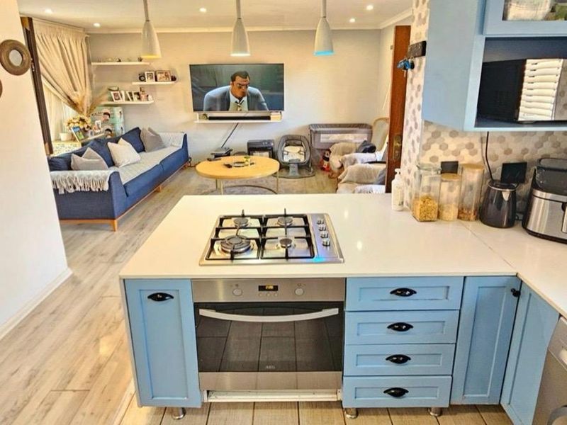Open-plan living area featuring a modern kitchen with blue cabinetry, quartz countertops, gas hob, and integrated oven, flowing into a comfortable lounge space.