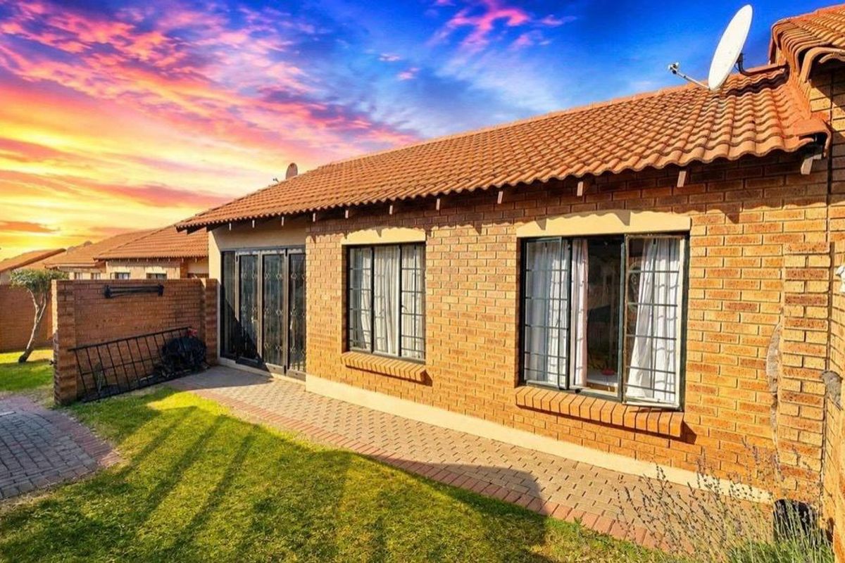 Rear view of a face-brick townhouse featuring a paved walkway, small garden area, and secure window and door fittings.