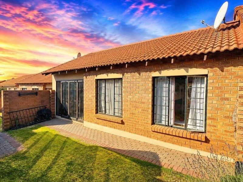 Rear view of a face-brick townhouse featuring a paved walkway, small garden area, and secure window and door fittings.