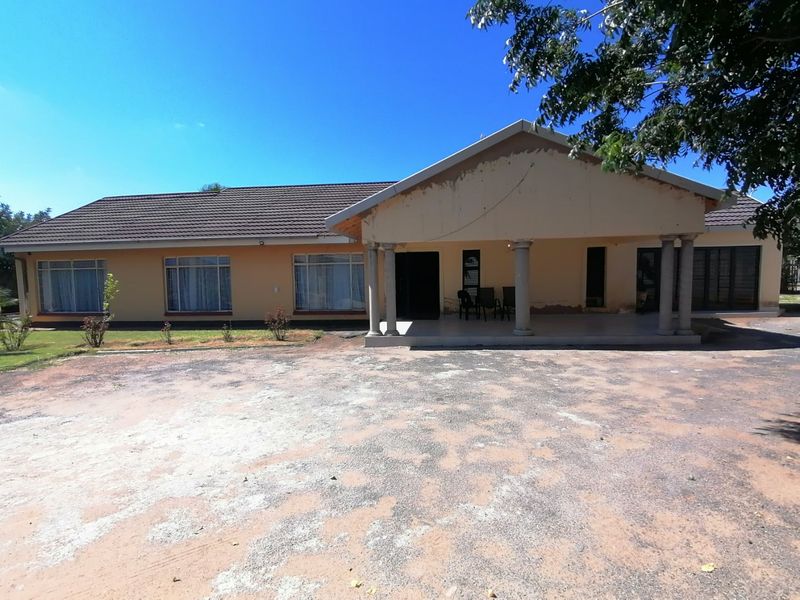 Front elevation of a single-story house featuring a covered patio with concrete columns, tiled roof, and an unpaved driveway area.