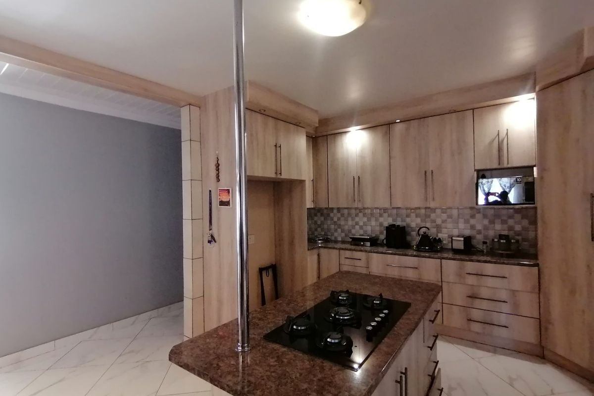 A functional kitchen featuring light wood-finish cabinetry, a central island with a built-in gas hob, stone countertops, and tiled flooring.