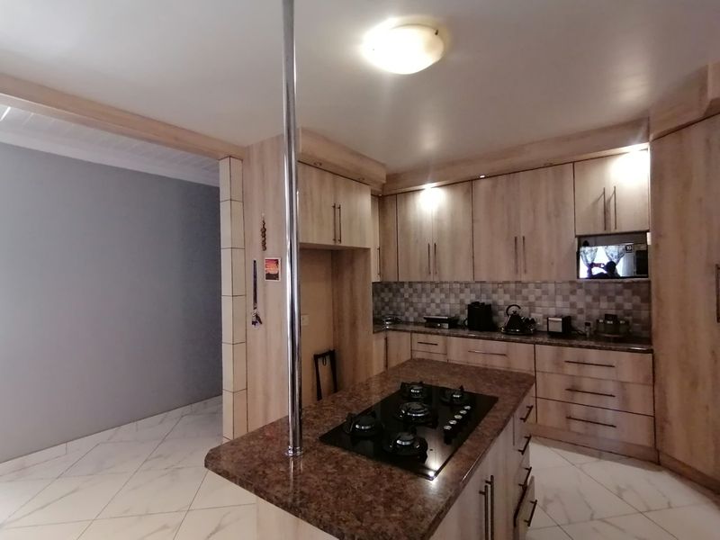 A functional kitchen featuring light wood-finish cabinetry, a central island with a built-in gas hob, stone countertops, and tiled flooring.