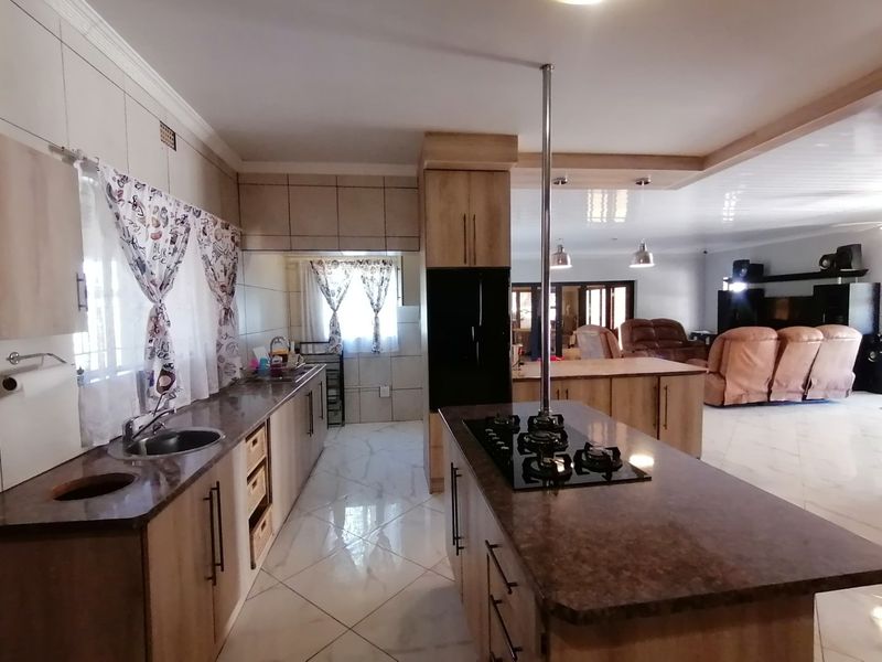 Spacious open-plan kitchen featuring a central island with a gas hob, stone countertops, and ample built-in cabinetry, flowing into the living area.