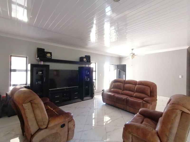 Spacious living room featuring glossy floor tiles, PVC ceiling panels, and a ceiling fan, offering a bright and functional layout.