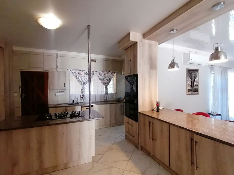 Spacious open-plan kitchen featuring modern wood-finish cabinetry, granite countertops, a gas hob, and a breakfast bar, seamlessly flowing into the living area.