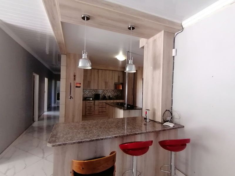 Open plan kitchen featuring wood-look cabinetry, granite countertops, a breakfast bar with pendant lighting, and tiled flooring throughout the living space.