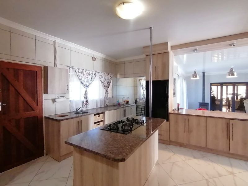 Spacious kitchen featuring a central island with a built-in gas hob, granite countertops, ample cabinetry, and tiled flooring, flowing into the adjacent living area.