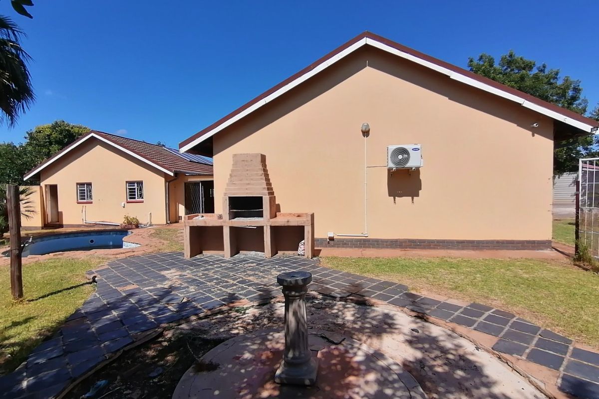 Rear exterior view featuring a swimming pool, tiled patio area with a built-in braai, and an air conditioning unit mounted on the wall.