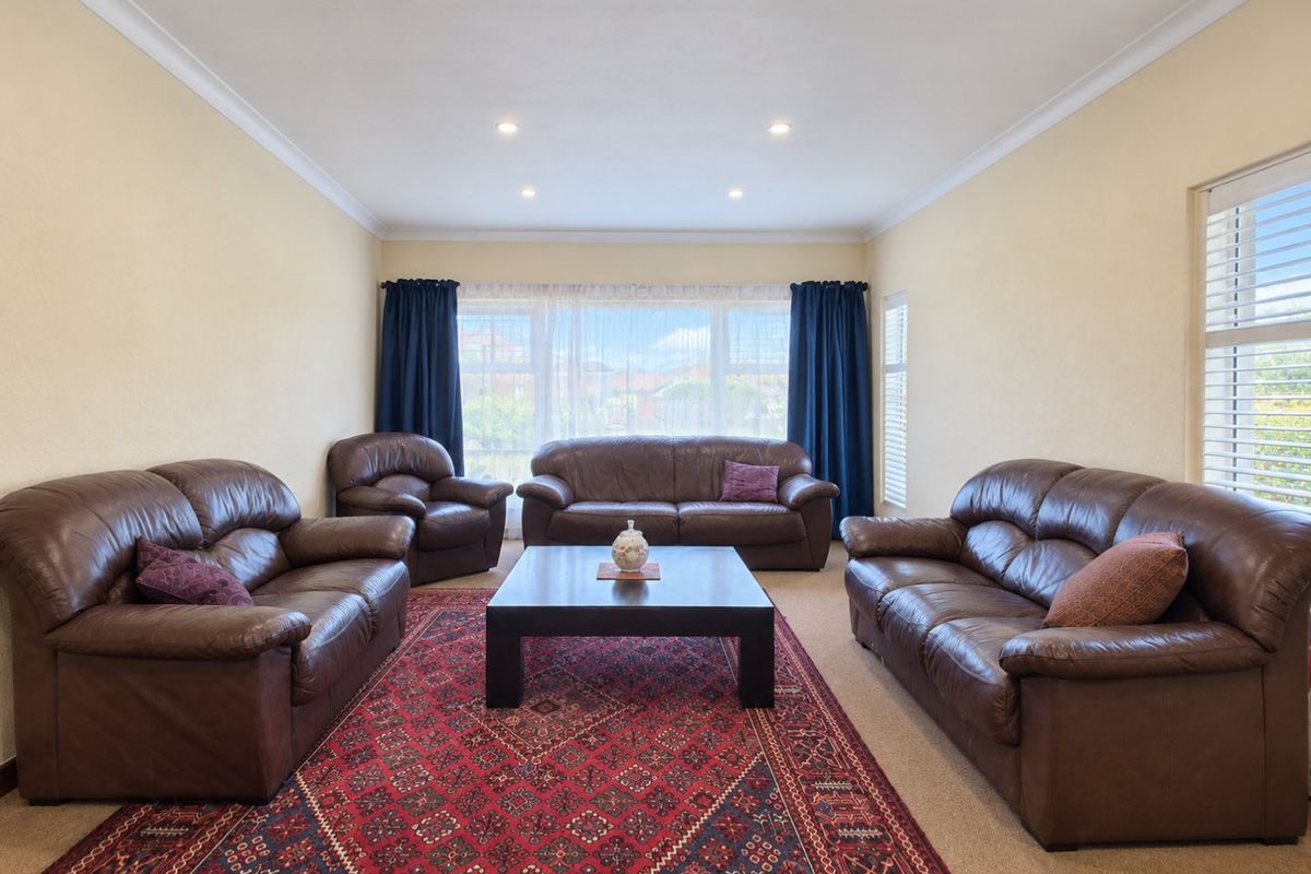 A spacious living room featuring recessed downlighting, decorative cove cornicing, and large windows fitted with plantation shutters, providing ample natural light.