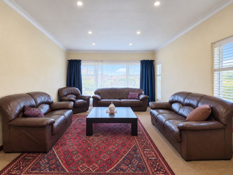 A spacious living room featuring recessed downlighting, decorative cove cornicing, and large windows fitted with plantation shutters, providing ample natural light.