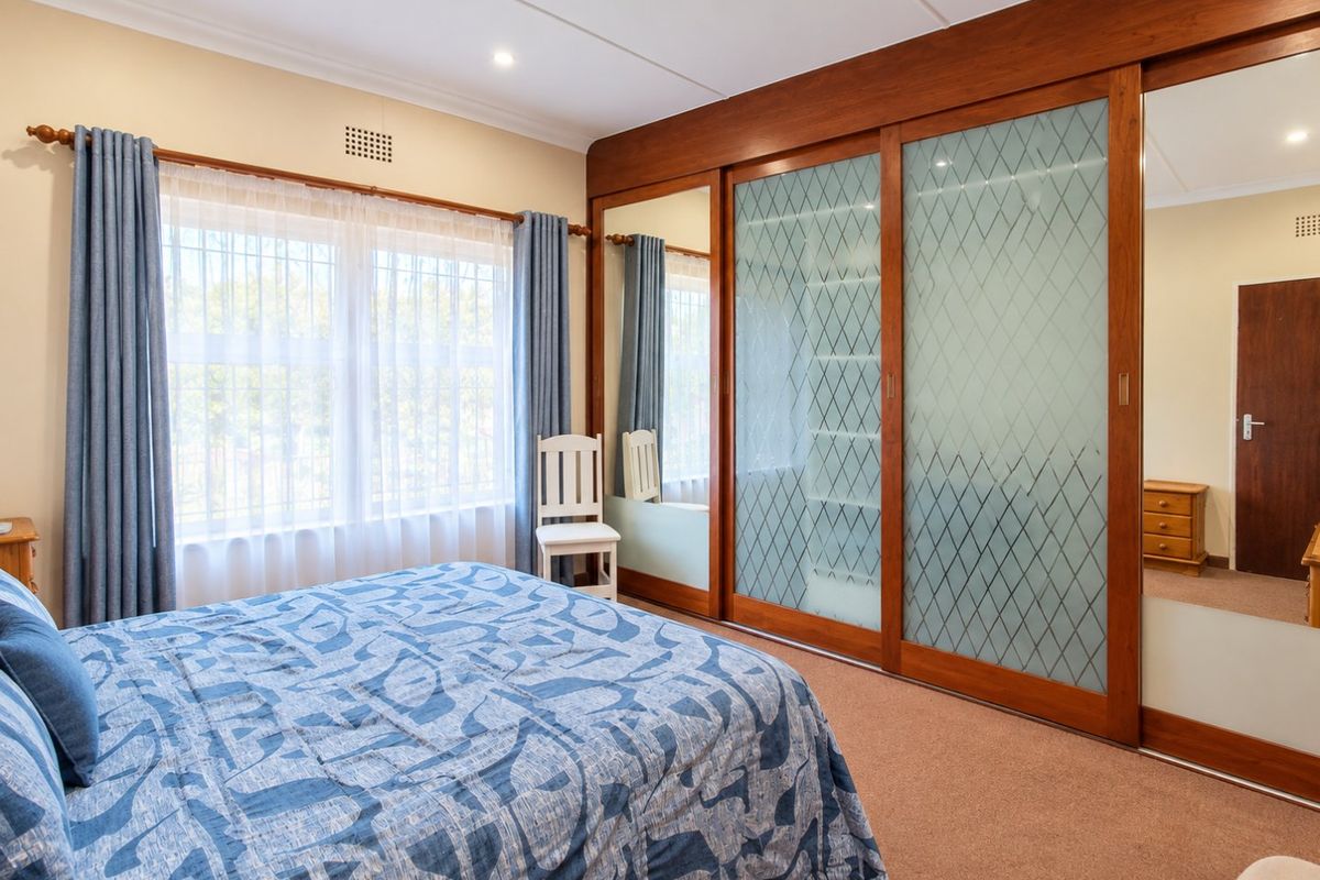 A well-maintained bedroom featuring extensive built-in wardrobes with mirrored and frosted glass sliding doors, recessed lighting, and neutral carpeting.