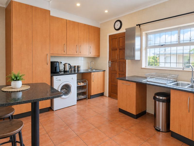 Functional scullery featuring wood-finish cabinetry, granite countertops, double stainless steel sink, and tiled flooring with integrated laundry appliance space.