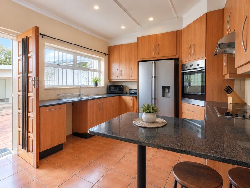 A functional kitchen featuring warm-toned wooden cabinetry, granite countertops, integrated stainless steel appliances, and direct access to an outdoor patio area.