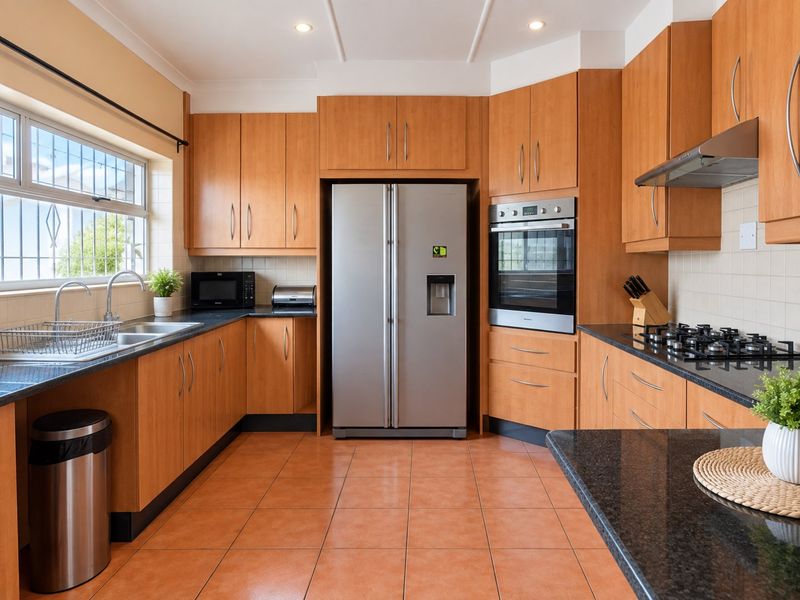 A functional kitchen featuring warm-toned wooden cabinetry, granite countertops, built-in oven, gas hob, and tiled flooring with ample storage space.