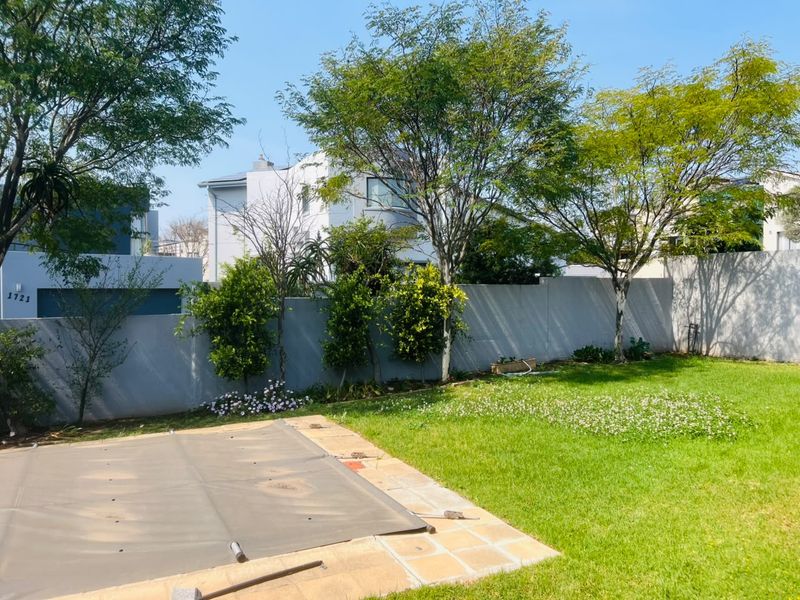 A private backyard featuring a swimming pool with a protective cover, paved surround, and a well-maintained lawn enclosed by a perimeter wall.