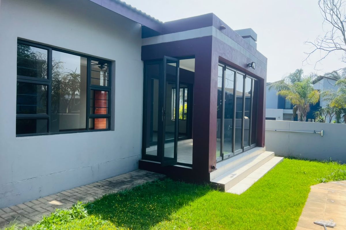 Rear exterior view of the house featuring a paved walkway, a small tiled patio area, and modern aluminium sliding doors leading into the living space.