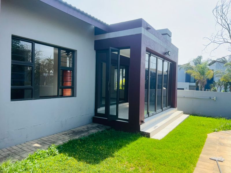 Rear exterior view of the house featuring a paved walkway, a small tiled patio area, and modern aluminium sliding doors leading into the living space.