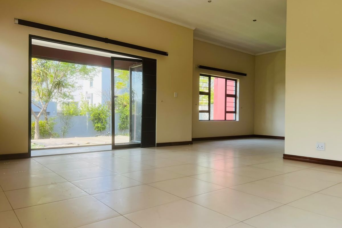 Spacious, light-filled living area featuring neutral tiled flooring, large sliding glass doors opening to the garden, and modern aluminium window frames.