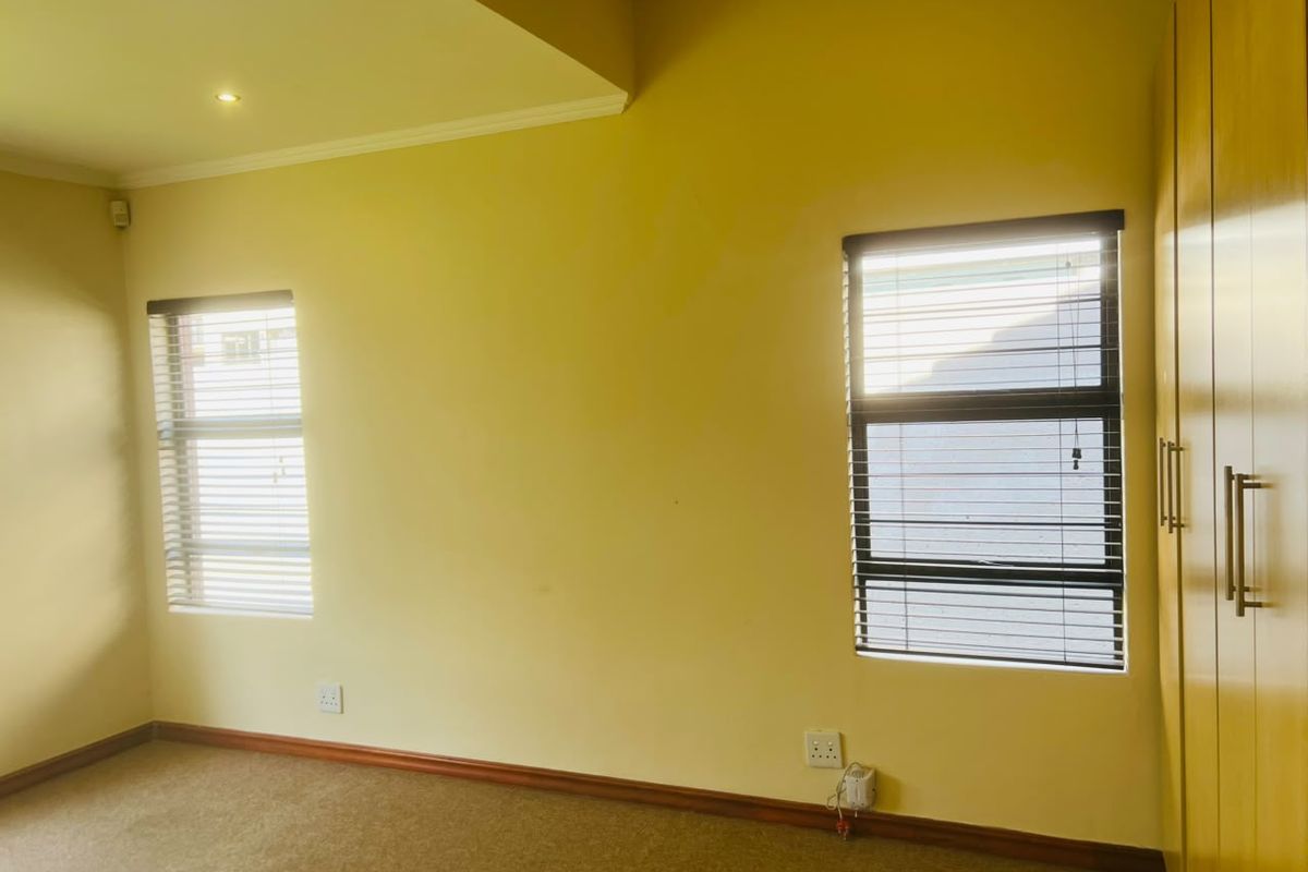 A bright, empty bedroom featuring built-in cupboards, carpeted flooring, and venetian blinds on the windows.