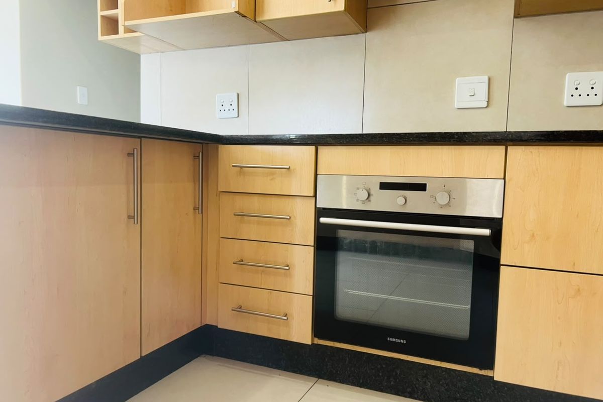 A clean, functional kitchen featuring light wood cabinetry, dark granite countertops, and a built-in stainless steel oven.