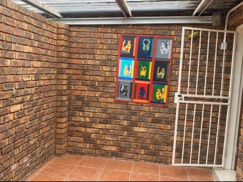 A covered outdoor patio area featuring face brick walls, tiled flooring, and a secure metal gate, providing a private and functional outdoor space.