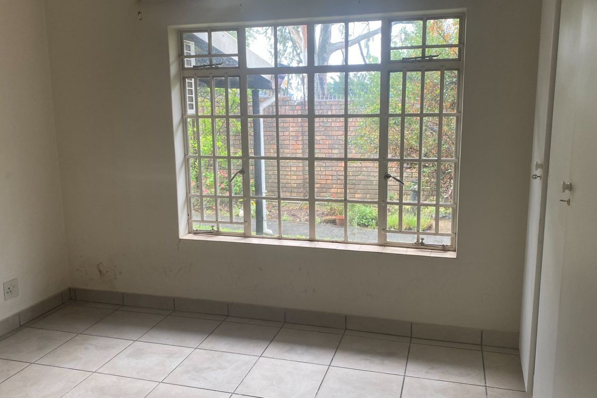 An empty bedroom featuring tiled flooring, a large window with security bars, and a built-in cupboard, offering a blank canvas for personalization.