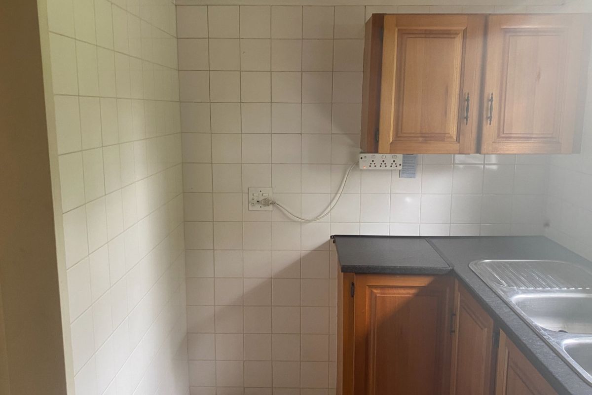 A compact kitchen area featuring wooden cabinetry, a double bowl stainless steel sink, and tiled splashbacks, presenting an opportunity for modernization.