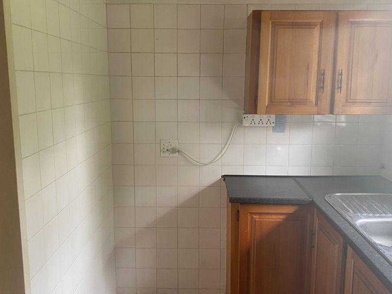 A compact kitchen area featuring wooden cabinetry, a double bowl stainless steel sink, and tiled splashbacks, presenting an opportunity for modernization.