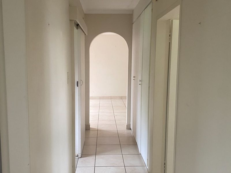 A bright, empty hallway featuring tiled flooring, built-in storage cupboards, and a classic arched transition leading into the main living area.