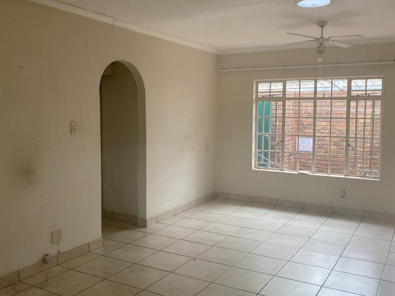 An empty living room featuring tiled flooring, a ceiling fan, a skylight, and an arched doorway leading to an adjacent space.