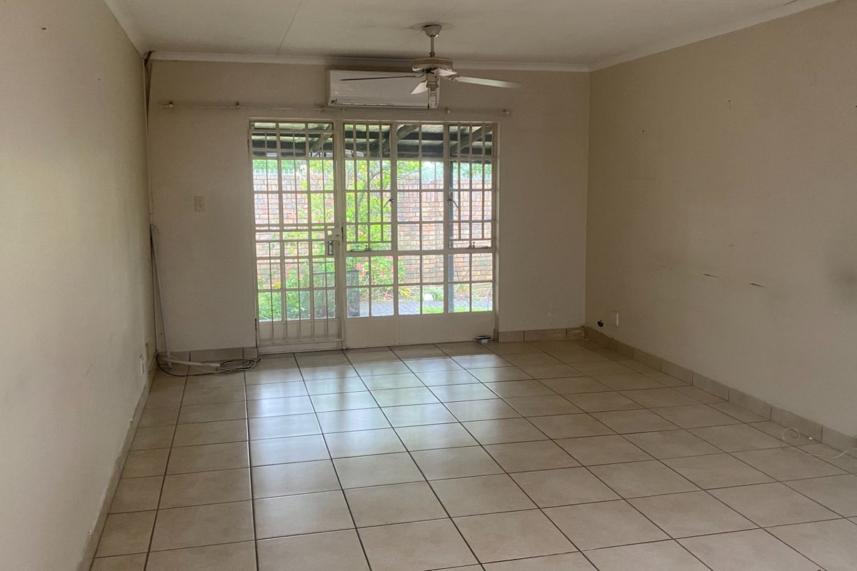 An empty living room featuring tiled flooring, a ceiling fan, a wall-mounted air conditioner, and a security gate leading to the exterior.