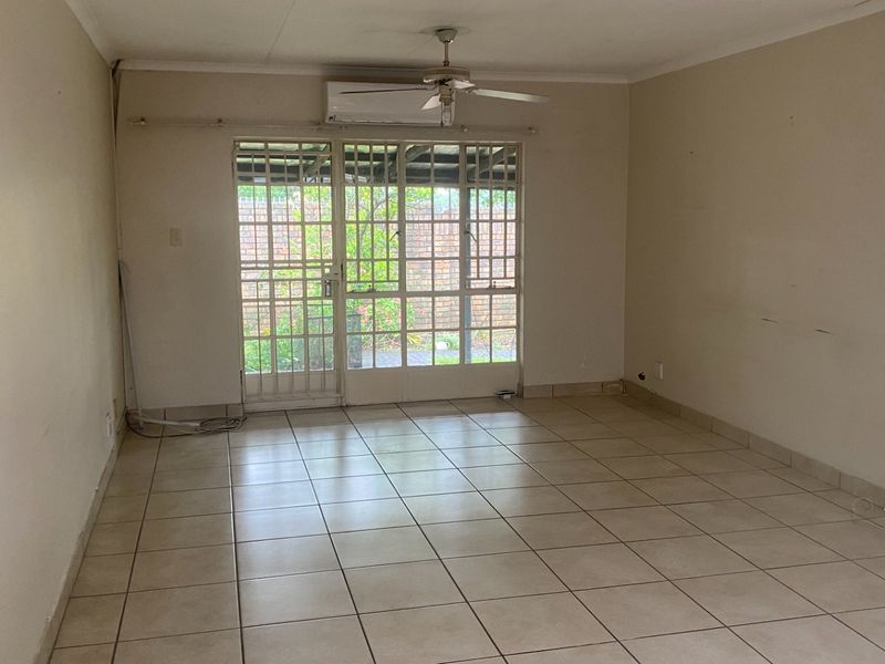 An empty living room featuring tiled flooring, a ceiling fan, a wall-mounted air conditioner, and a security gate leading to the exterior.