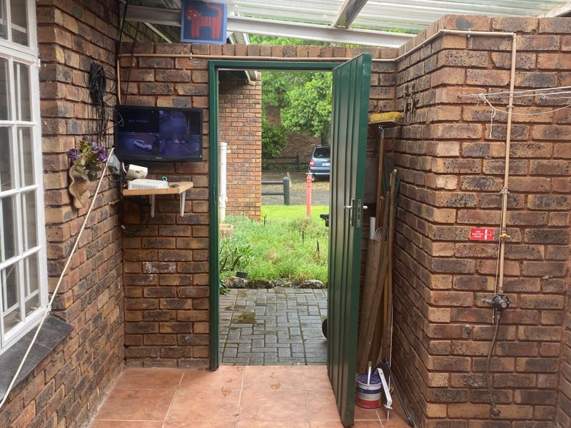 A functional utility space featuring exposed brick walls, tiled flooring, and a translucent roof, providing direct access to the exterior garden area.