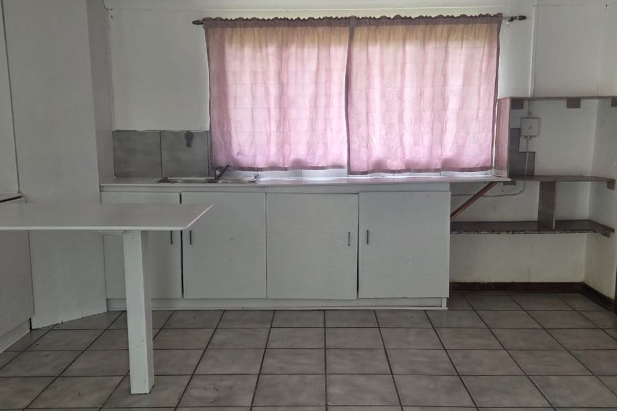 A functional kitchen space featuring built-in cabinetry, a stainless steel sink, tiled flooring, and a wooden door, ready for modernization and renovation.