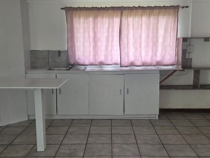 A functional kitchen space featuring built-in cabinetry, a stainless steel sink, tiled flooring, and a wooden door, ready for modernization and renovation.