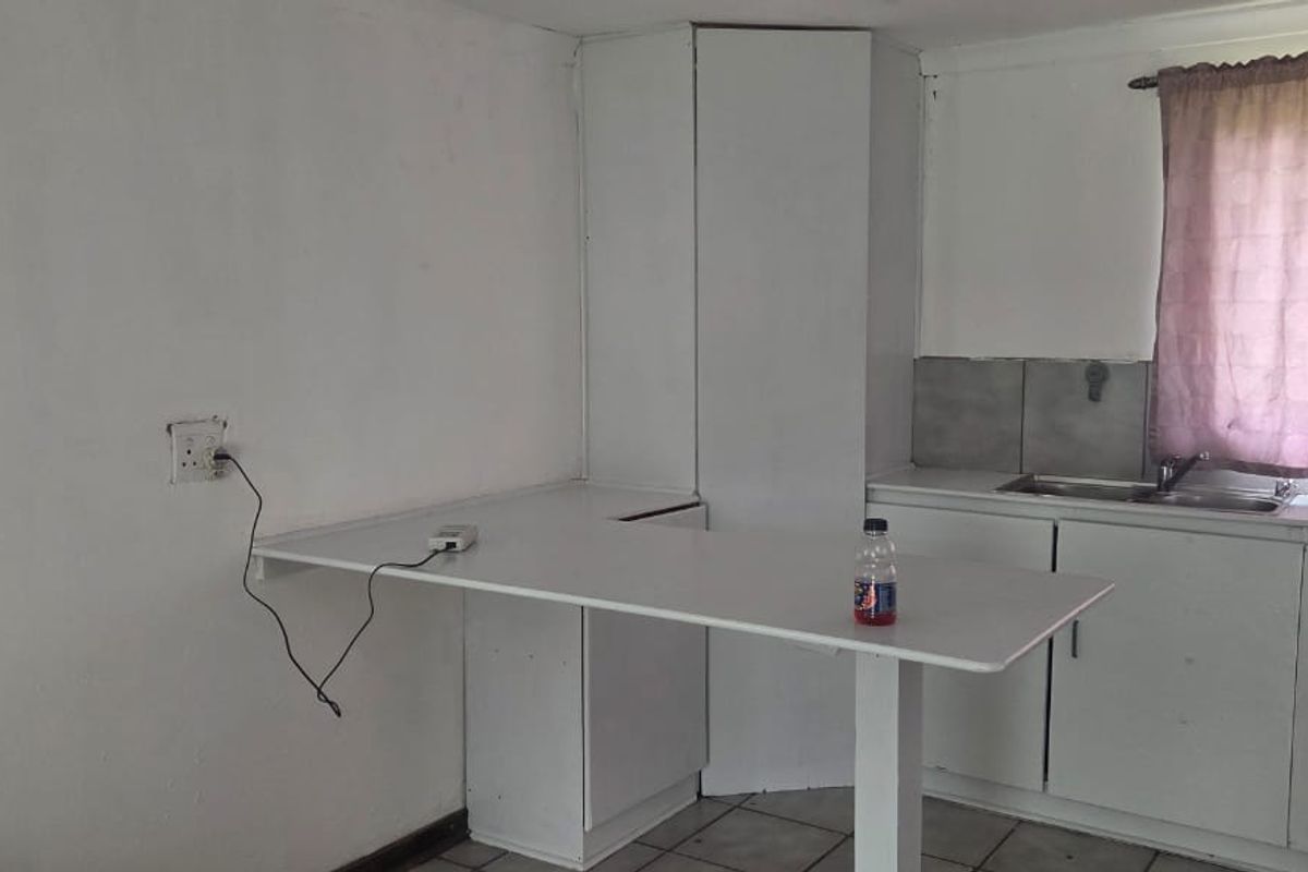 A basic kitchen area featuring built-in white cabinetry, a stainless steel sink, tiled backsplash, and a breakfast counter, requiring cosmetic updates.
