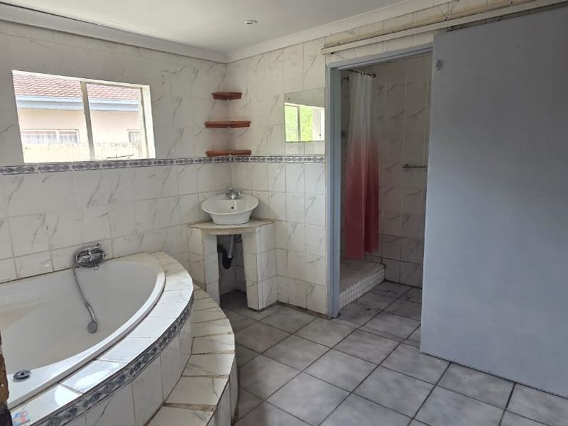 A dated bathroom featuring a corner bathtub, vessel sink, and separate shower area with tiled finishes throughout.