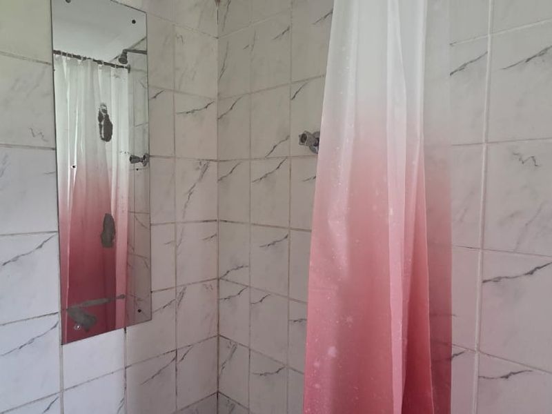 A bathroom shower area featuring marble-effect wall tiles, a wall-mounted shower head, and a towel rail, currently showing signs of wear and aging.