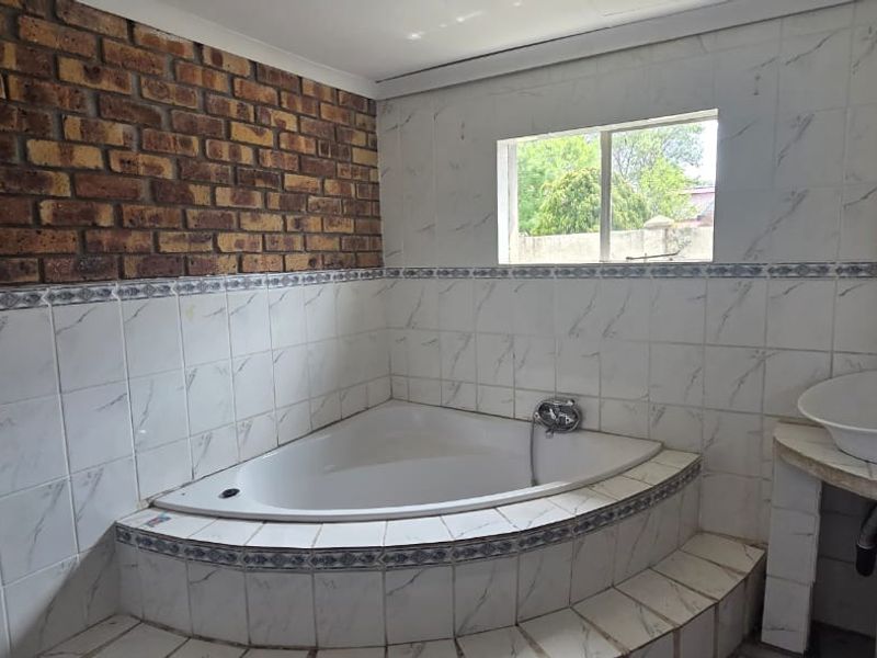 Bathroom featuring a corner bathtub, pedestal washbasin, and a combination of tiled walls and an exposed brick feature wall.