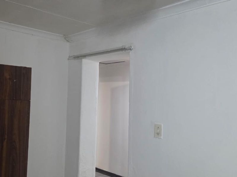 A bedroom interior featuring a built-in wooden cupboard, cove cornicing, and a doorway leading to an adjacent space.