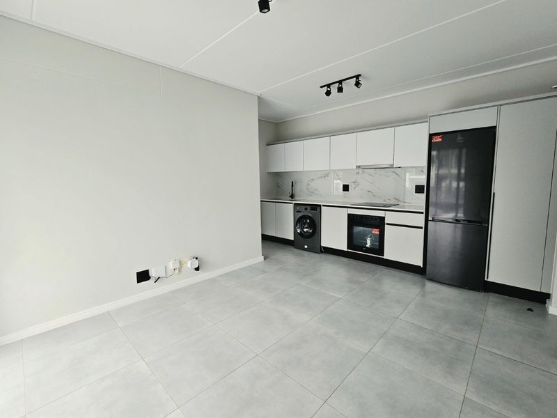 Modern open-plan kitchen featuring sleek white cabinetry, marble-look splashback, integrated appliances, and contemporary track lighting, set against neutral tiled flooring.