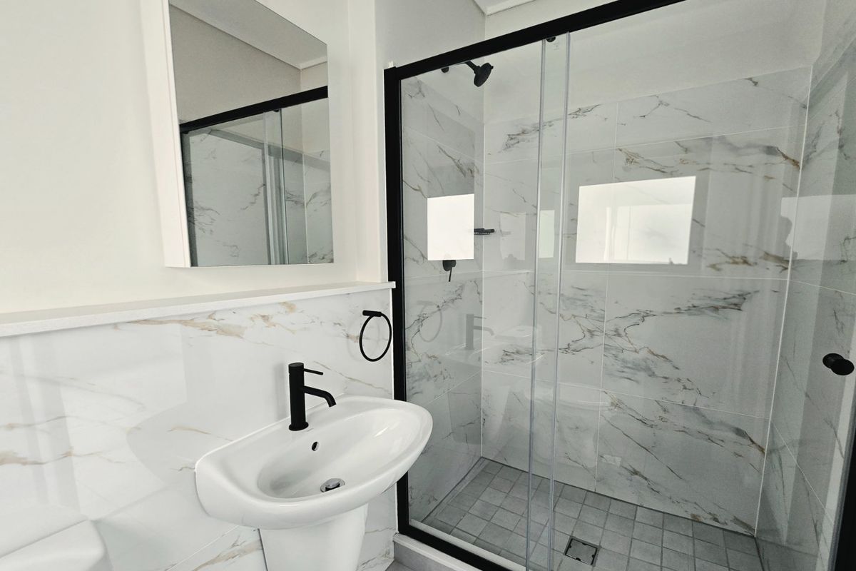 Modern bathroom featuring a walk-in shower with black frame, marble-look wall tiles, and a sleek pedestal basin with black mixer tap.