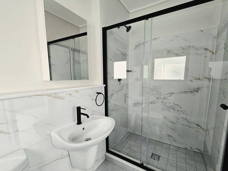 Modern bathroom featuring a walk-in shower with black frame, marble-look wall tiles, and a sleek pedestal basin with black mixer tap.